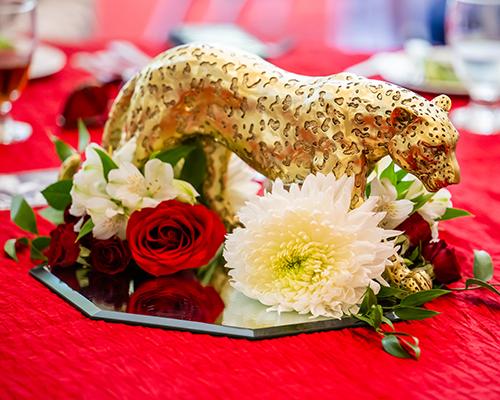 Golden jaguar statue on mirror plate surrounded by flowers.