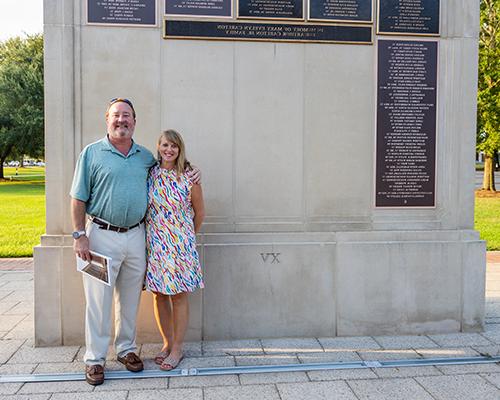 Two alumni in front of the Wall of Honor on campus.